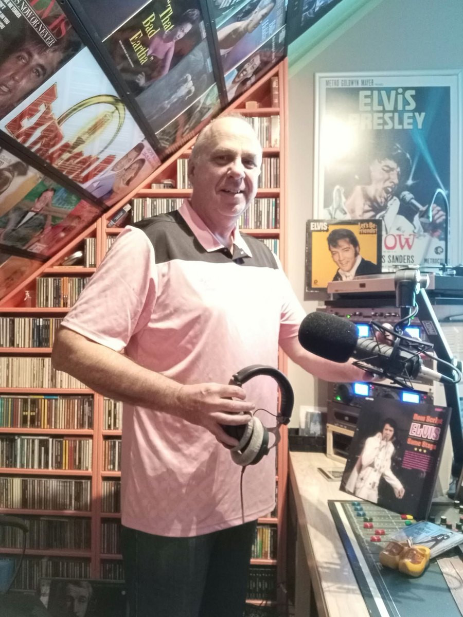 Fred van Veen in zijn studio, met een koptelefoon in zijn hand en zijn platenverzameling achter zich